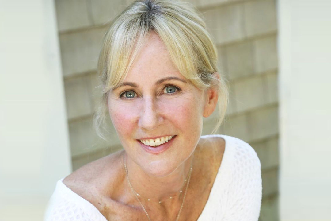 Woman with her hair tied back and a white v neck shirt smiling broadly